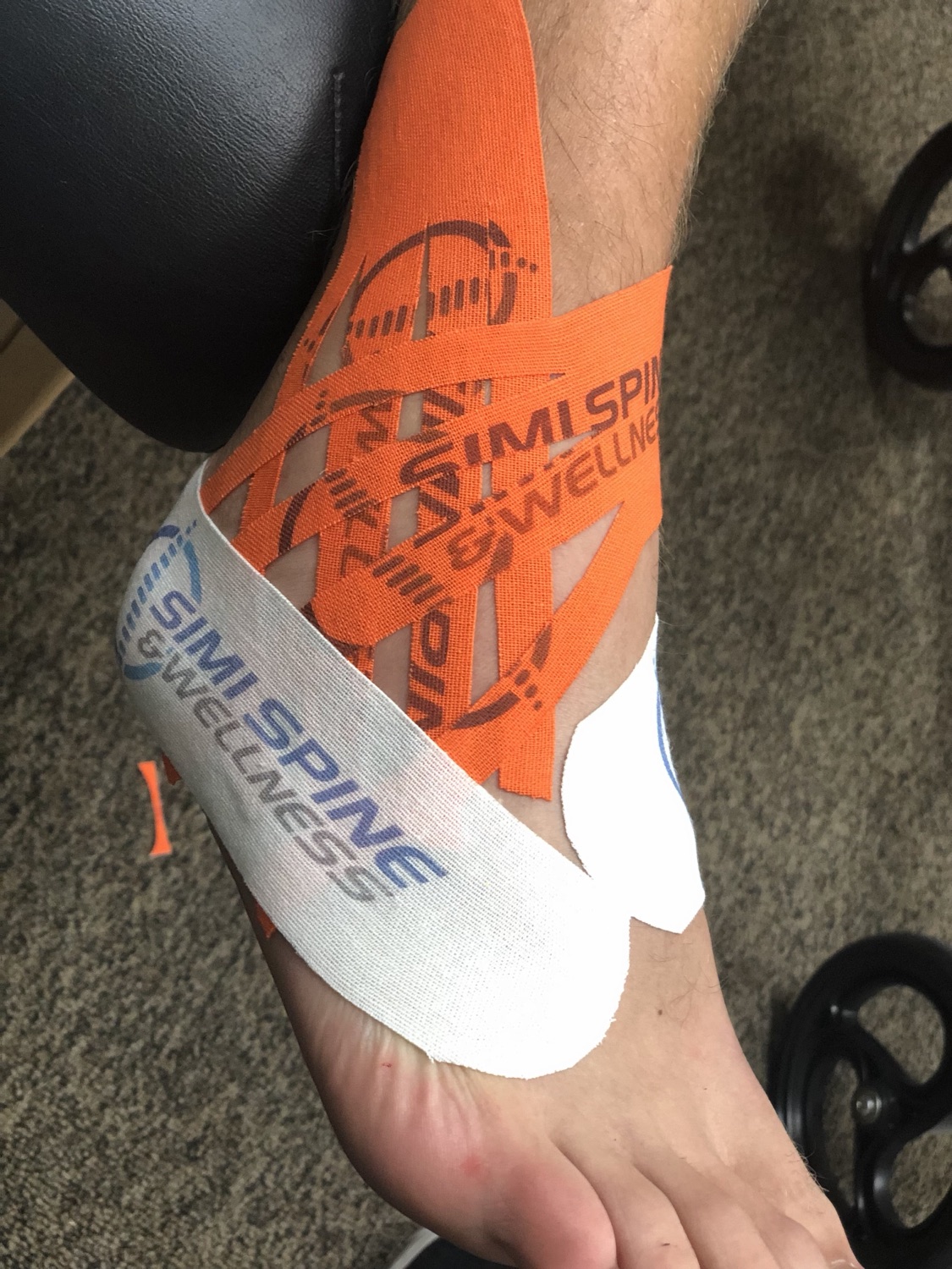 Kinesiology taping on an ankle using Simi Spine & Wellness branded tape